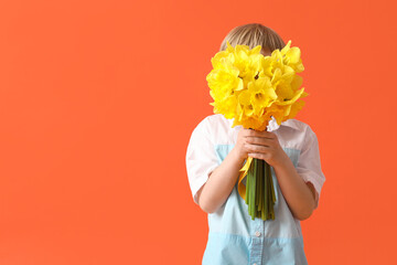 Cute little happy boy with bouquet of beautiful narcissus on orange background