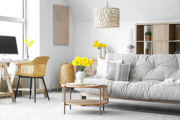 Interior of stylish living room with sofa, coffee table and vase of narcissus flowers