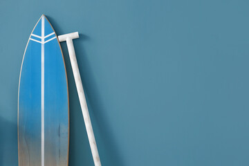 Wooden surfboard with paddle near blue wall