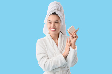 Young Asian woman in bathrobe with soap on blue background