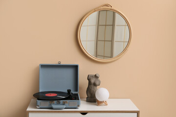 Record player with disk and home decor on commode near beige wall in room