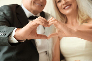 Mature couple making heart gesture on their wedding anniversary at home, closeup