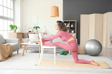 Sporty mature woman with chair doing yoga at home