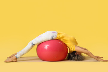 Sporty mature woman doing yoga on fitball against yellow background