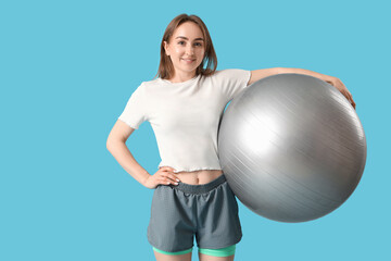Sporty young woman with fitball on blue background