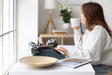 Young woman with vintage typewriter drinking coffee at home