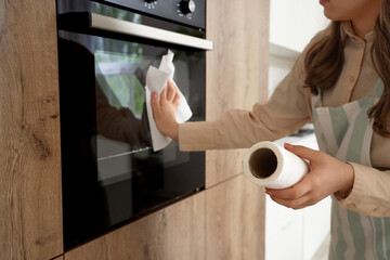 Housewife wiping oven with paper towel in kitchen, closeup