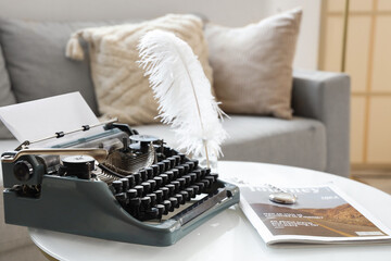 Vintage typewriter with feather and magazine on table in living room, closeup