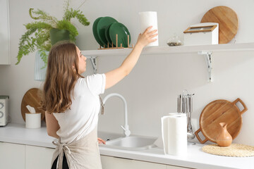 housewife taking roll of paper towels from shelf in kitchen