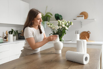 Young woman wiping flowers with paper towel in kitchen