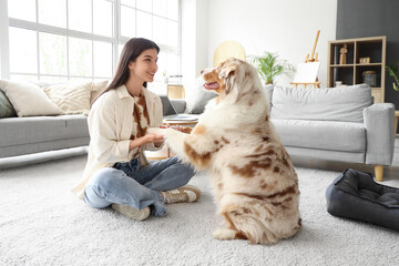 Young woman holding Australian Shepherd dog's paws at home