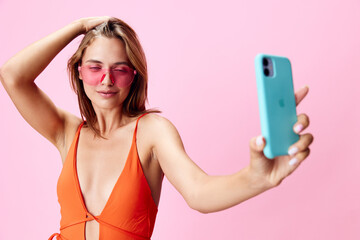 Vibrant woman in orange swimsuit capturing a moment with cell phone on bright pink background