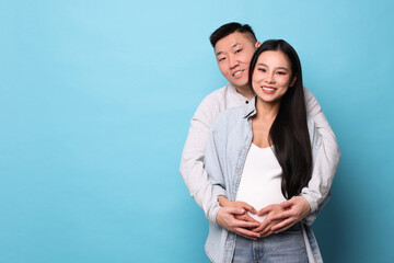 Man touching his pregnant wife's belly on light blue background, space for text