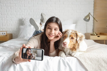 Young woman with Australian Shepherd dog taking selfie in bedroom