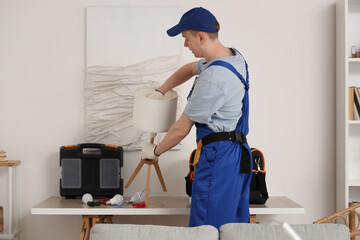 Male technician repairing lamp in room