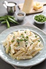 Delicious pasta with green peas, cheese, creamy sauce and ground pepper on grey table