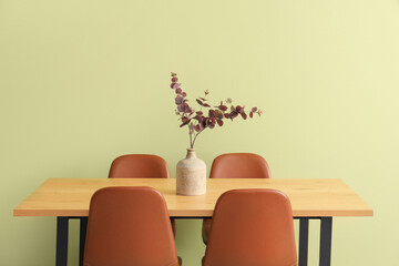 Vase with artificial eucalyptus branches on dining table near green wall