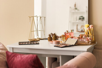 Makeup products with jewelry and mirror on table in dressing room