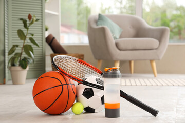 Sports water bottle with racket and balls on floor in living room, closeup