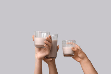 Female hands with glasses of tasty chocolate milk on grey background