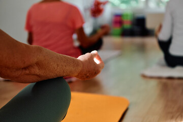 In this sunlit space, a senior woman's hand gracefully engages in various yoga poses, embodying the...