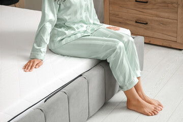 Young woman sitting on soft mattress in bedroom