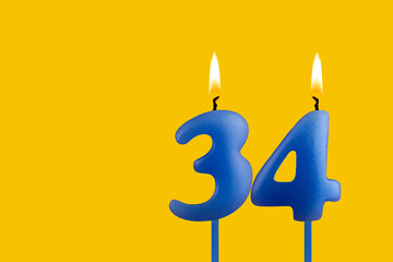 Blue birthday candle on yellow background - Number 34
