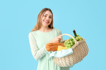 Beautiful young happy woman with food and bottle of wine for picnic in wicker basket on blue...
