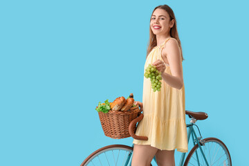 Beautiful young happy woman with bicycle and wicker picnic basket of tasty food on blue background