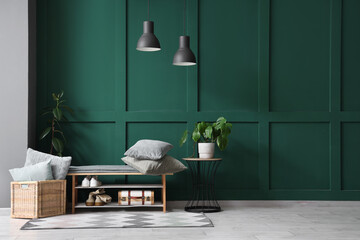 Cozy bench, shoes, pillows and lamp near green wall in beautiful room