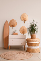Surfboard, houseplant and chest of drawers near white wall in room