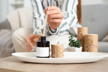 Young woman with reed diffuser on table at home