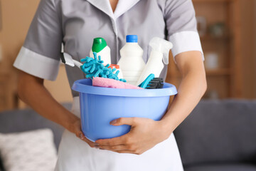 Young chambermaid with cleaning supplies in room, closeup