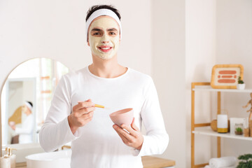 Young man with applied clay mask in bathroom