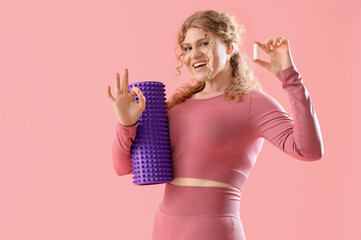 Female trainer with foam roller and tampon showing OK on pink background