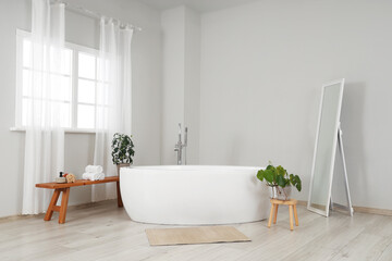 Interior of light room with bathtub, plants and mirror
