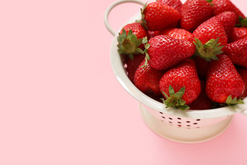 Colander with sweet fresh strawberries on pink background