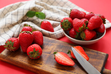 Wooden board and bowl with sweet fresh strawberries on red background