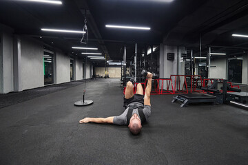 A muscular man is focused on working out with dumbbells in a modern gym, showing his determination...
