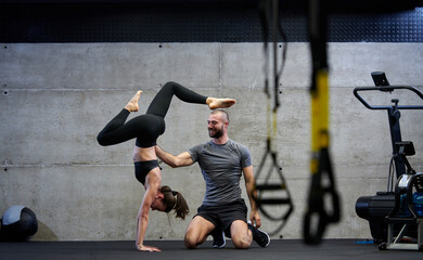 A muscular man assisting a fit woman in a modern gym as they engage in various body exercises and...