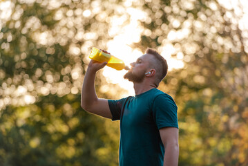 A fit young man drinking water from a bottle after a run or workout active healthy lifestyle.