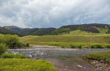 Rio Grande river headwaters with green hills and overcast skies
