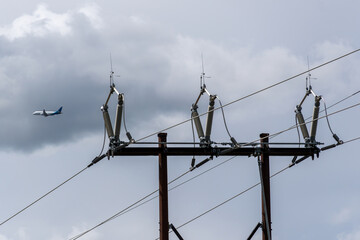 Substation power grid pointing upward with commercial airplane flying in the sky.