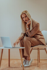 A professional businesswoman sits on a chair, surrounded by a serene beige background, diligently...