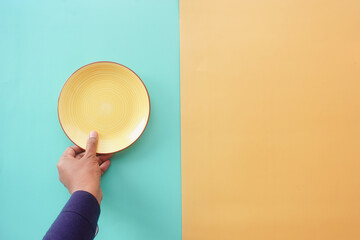 Hand Holding Yellow Plate on Split Color Background