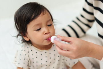 mother feeding liquid medicine to sick toddler girl with dropper
