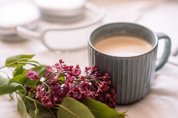 Cup of coffee with a sprig of lilac in front of wireless headphones on a white background.