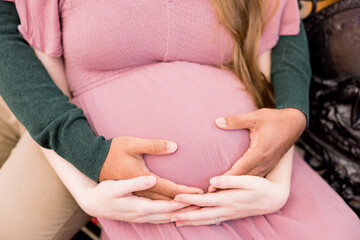 A man is cradling his pregnant wife's belly while they sit down. 