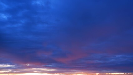 A breathtaking sunrise with a deep blue sky transitioning to shades of purple and pink near the horizon. The clouds are dark but tinged with warm hues, creating a dramatic and serene atmosphere.
