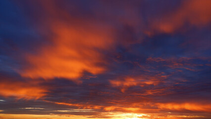 A stunning sunrise with vibrant hues of orange and red blending into the darker blues of the sky. The clouds are dramatically illuminated, creating a warm, fiery atmosphere. Sunrise sky background.
